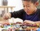 Jeune garçon asiatique en t-shirt à manches longues bleu marine jouant avec de nombreuses petites voitures colorées sur la table en bois d'un salon